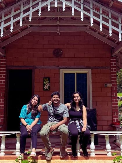 Three travelers relaxing on the porch of a charming brick cottage in Chikmagalur.