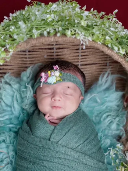 A slightly different angle showing the baby peacefully sleeping, wrapped snugly in a green swaddle against a rich, dark backdrop.