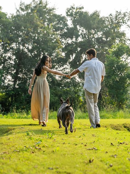 A beautiful action shot of an engaged couple walking hand-in-hand through a grassy field, with their happy pitbull, Millie, leading the way.