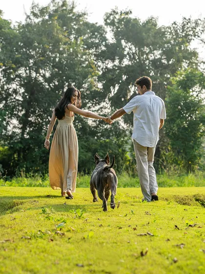 A beautiful action shot of an engaged couple walking hand-in-hand through a grassy field, with their happy pitbull, Millie, leading the way.