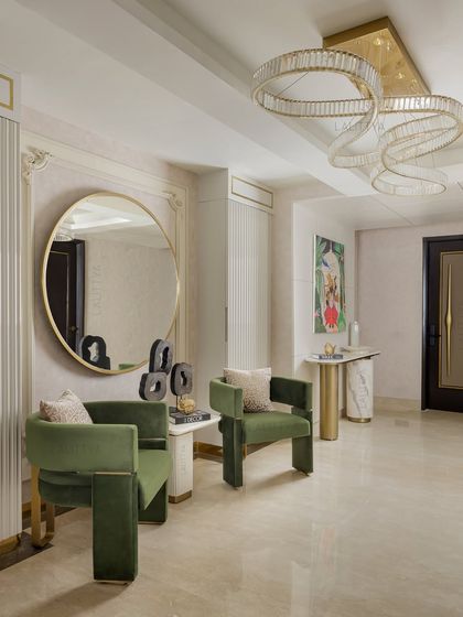 A wider view of the sophisticated foyer, showcasing the pairing of bold green chairs, a spiral chandelier, and a minimalist console table, creating a grand first impression.