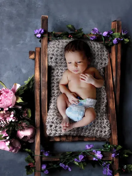 A 17-day-old newborn lying on a miniature ladder prop decorated with purple flowers.