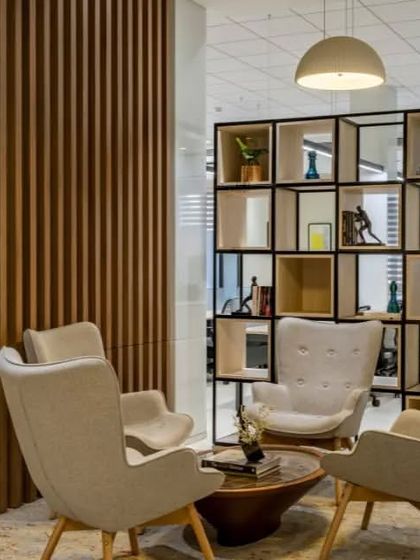 A semi-private breakout area for informal meetings or a quiet break. The slatted wood partition provides visual separation, while the geometric shelving unit adds a modern, decorative touch.