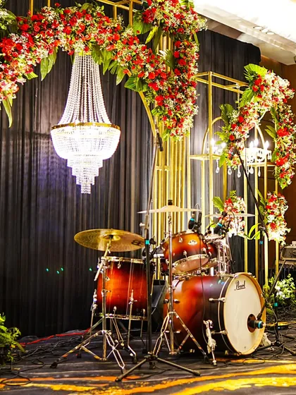 The stage is set for a memorable performance. A grand crystal chandelier hangs above the drum kit, framed by golden arches and rich red floral arrangements for a 60th birthday bash.