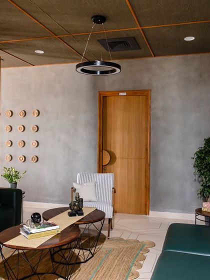 The lounge area at Anthea Pharma, subtly divided by a striking wooden partition. The ceiling is adorned with a traditional chattayi design, balancing the industrial tones of the concrete with Indian craftsmanship.