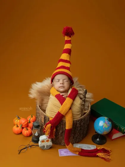 A creative Harry Potter inspired newborn shoot. The baby is wrapped snugly in a basket with a striped scarf, a magic wand, and other themed props for a truly magical first portrait.