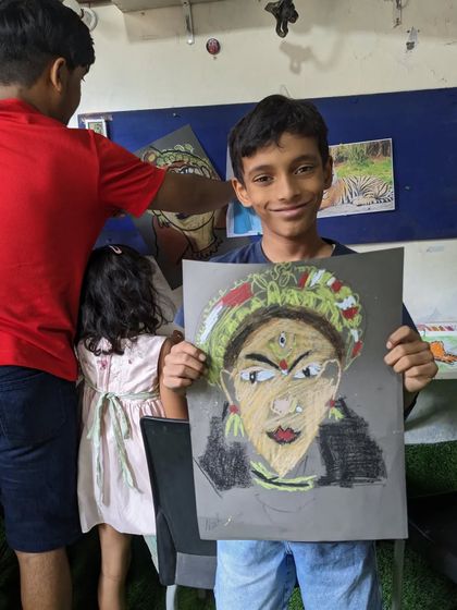 A student smiling with his finished portrait, inspired by traditional Indian performance art. The use of color and detail in the headwear is fantastic.