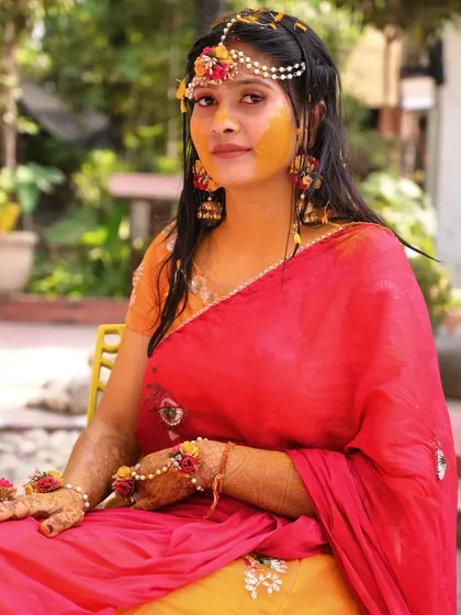 A beautiful portrait of the bride adorned with floral jewelry and haldi, looking directly at the camera with a gentle expression.