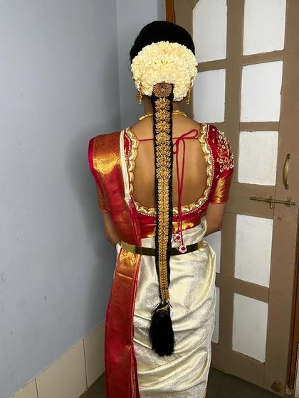 The back view of Vathsala's Muhurtham hairstyle, featuring a traditional braid with jasmine flowers and gold hair ornaments, perfectly complementing her classic white and red saree.