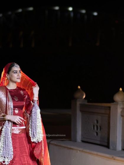 A clean, beautiful shot of Kriti Sanon in a crimson Banarasi silk lehenga, looking ethereal against the night sky and festive lights.