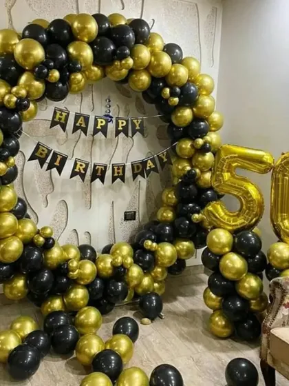A grand 50th birthday party backdrop. This impressive setup includes a large circular arch made of black and gold chrome balloons, a 'Happy Birthday' banner, and giant gold foil number balloons.