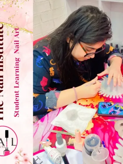 A student uses a fine brush to practice a detailed nail art design, with her phone nearby for inspiration.