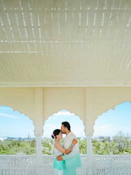 A serene pre-wedding portrait taken in a beautiful white pavilion with scalloped arches. The composition is clean and symmetrical, highlighting the couple's embrace against the lush green view.