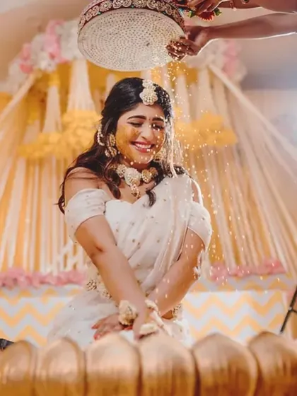 A candid shot from the Haldi ceremony, where the bride is showered with flowers. The yellow and white decor in the background adds to the festive atmosphere.