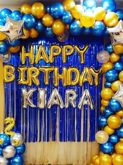 A classic half-arch balloon decoration for a birthday. The blue and gold chrome balloons with a fringe curtain backdrop make a great photo corner for any party.