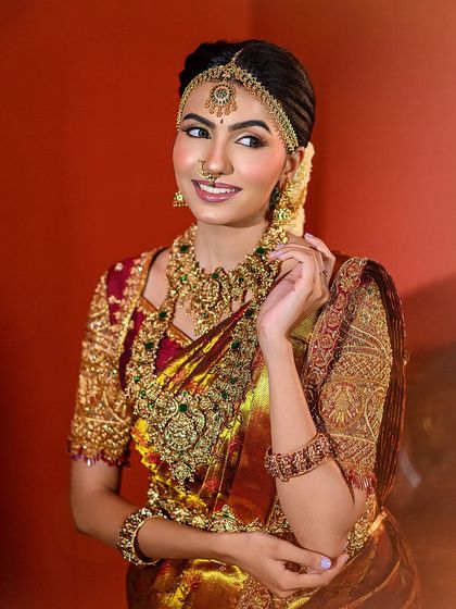 A joyful muhurtham look, capturing a bride's happy smile. The warm lighting enhances the golden tones of her saree and the intricate temple jewellery, creating a festive and radiant portrait.