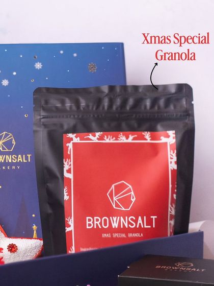 This shot features our Xmas Special Granola, with its festive red and white packaging. It's a unique and healthy treat that sets our holiday hampers apart from the rest.