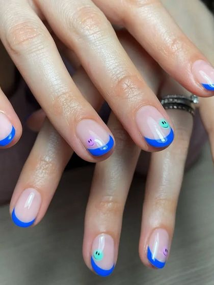 A fun and cheerful French manicure with bright blue tips and small smiley faces on the accent nails.