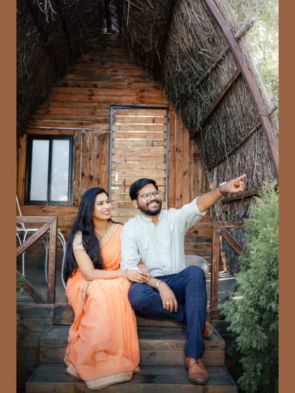 A candid moment on the porch of a rustic wooden cabin. The groom points towards their future, sharing a laugh with his bride-to-be in this natural and joyful pre-wedding photograph.