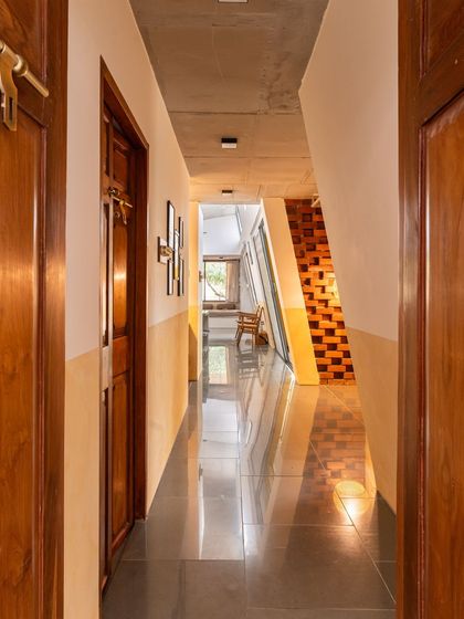 The main corridor of the house, with its polished floor reflecting the light from the inclined wall. The two-tone paint finish adds visual interest while maintaining the home's earthy and minimalist feel.