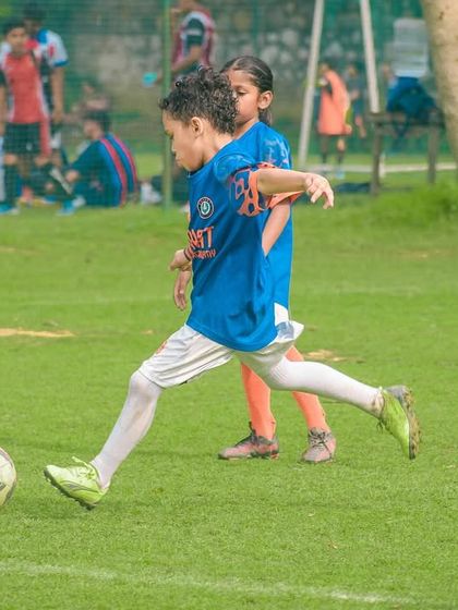 A young girl participates in a match, dribbling the ball forward while a teammate provides support from behind.