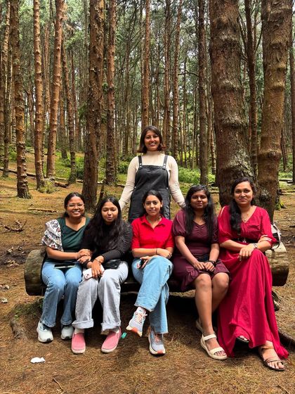 A group of girls sitting on a log in the pine forest.