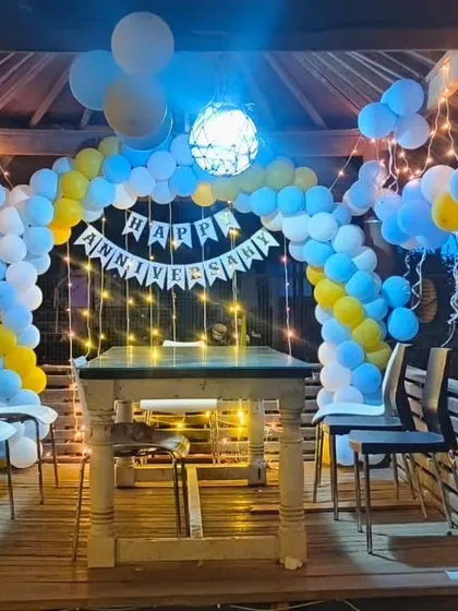 A cozy anniversary decoration for a gazebo or balcony, with a blue, white, and yellow balloon arch and fairy lights.