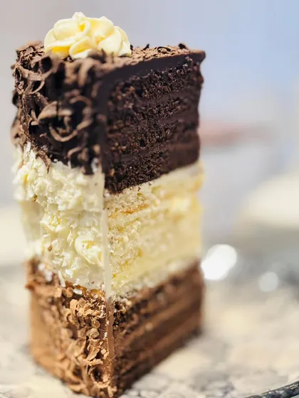 A slice of our signature 24-layer Triple Chocolate Heaven Pastry. It features distinct layers of dark, milk, and white chocolate mousse and sponge, creating an incredible texture and a rich, indulgent experience for any true chocolate lover.