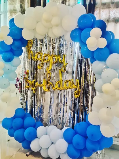 A simple and clean birthday decoration with a blue and white balloon ring against a silver tinsel backdrop.