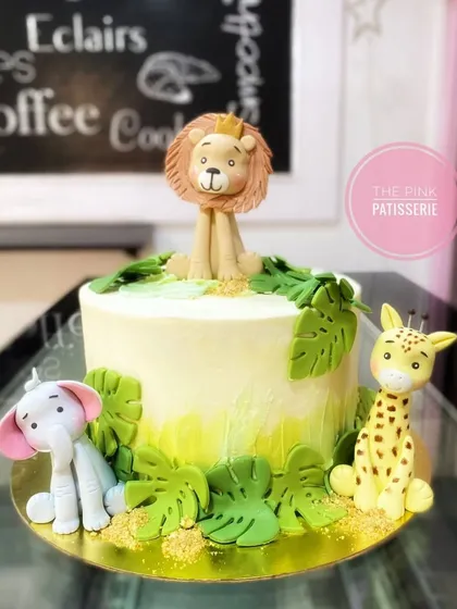 An elegant safari cake with beautifully crafted fondant animals. A crowned lion sits atop the cake, joined by a gentle elephant and a giraffe.