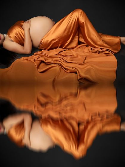 Embracing the pregnancy glow, this portrait captures the mom-to-be lying peacefully in a golden satin gown. The reflection on the floor doubles the beauty of this serene moment.