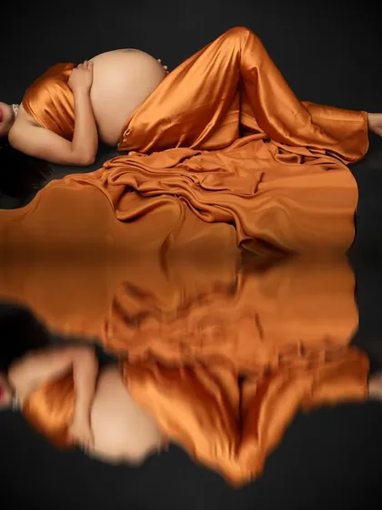 Embracing the pregnancy glow, this portrait captures the mom-to-be lying peacefully in a golden satin gown. The reflection on the floor doubles the beauty of this serene moment.