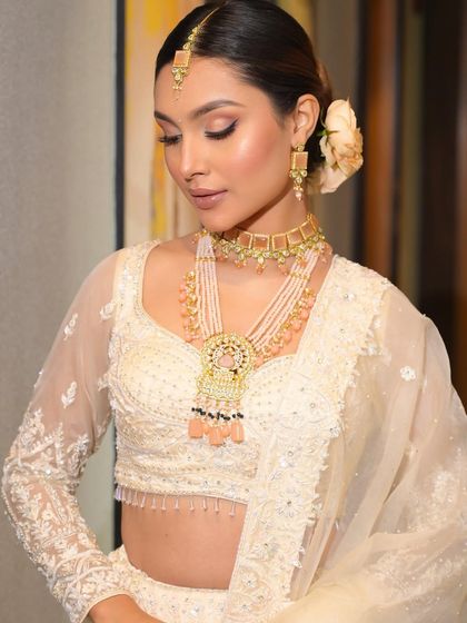 A close-up of the all-white bridal look, focusing on the delicate jewelry and the soft, peachy tones used in the makeup.