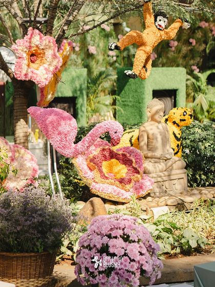 Another view of the whimsical floral animal sculptures, including a pink flamingo and a tiger, set against a lush green background.