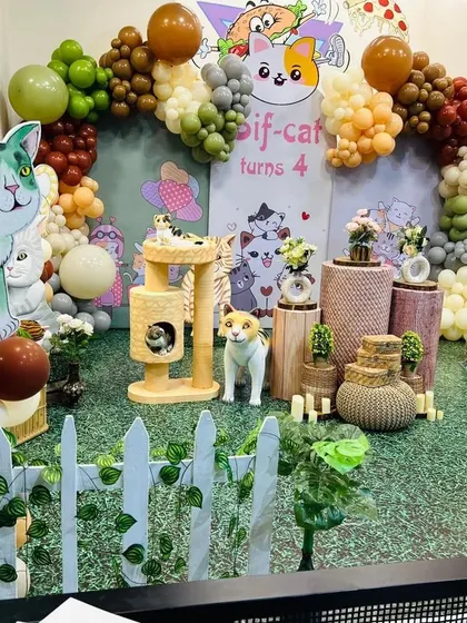 A wider view of the cat party, showing the artificial grass flooring and white picket fence that complete the garden-like setting.