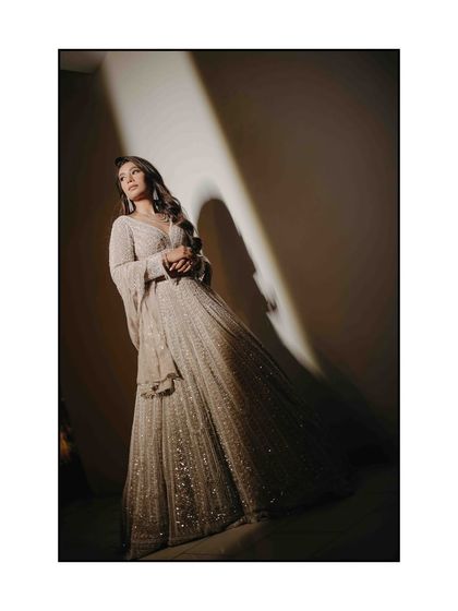 A full-length bridal portrait using dramatic lighting. The strong diagonal light creates long shadows, adding a sense of drama and elegance to this stunning shot of the bride in her shimmering gown.