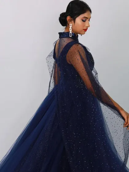 A side view of the navy blue caped ball gown, showing the beautiful drape of the sheer, sparkling cape.