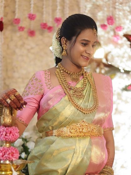 A serene and beautiful shot of Savitha at her baby shower. Her makeup is soft and glowing, perfectly complementing her pink and green silk saree.
