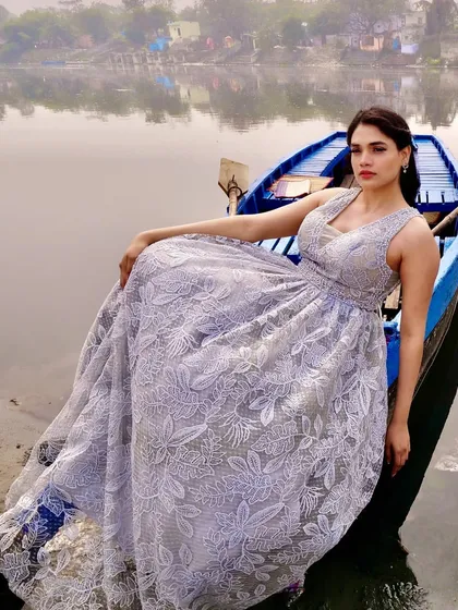 This shot shows the full volume of the embroidered lace gown as the model sits in a boat. The light grey color offers a unique and sophisticated alternative to traditional white, perfect for creating a memorable, artistic look.