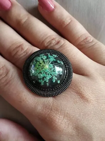 This adjustable ring features Queen Anne's lace, with its delicate, star-like pattern. The flower is set against a dark background, which makes the intricate details of the green and white petals stand out.