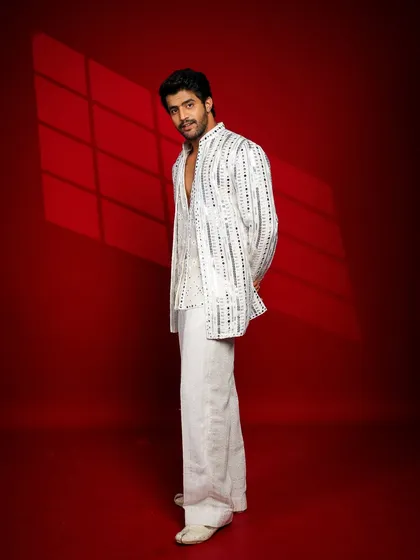 A stylish full-length shot of a male model in an elegant ethnic outfit. The side profile and subtle smile create a cool, confident look.
