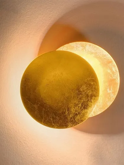 An eclipse-style wall light with a textured gold leaf finish. The light creates a beautiful corona effect, making it a stunning piece of wall decor.