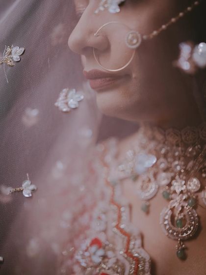 An artistic close-up through the veil, creating a soft, dreamy effect that highlights the bride's nose ring and the floral details on the fabric.