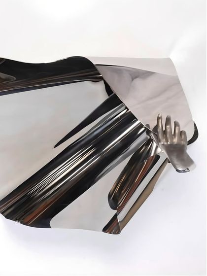 "The Power of Being," a freestanding stainless steel sculpture that merges an abstract, flowing sheet of metal with a figurative human hand.