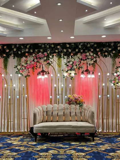 A vibrant stage with red backlighting and hanging floral arrangements. The modern scalloped sofa completes this stylish look, perfect for a contemporary wedding party.