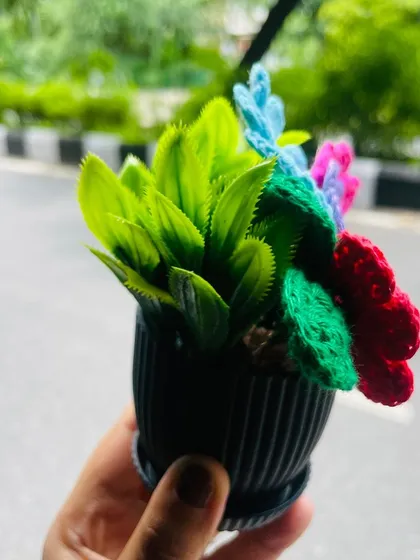 A side view of the rainbow flower pot, showing the artificial green leaves mixed in with the crochet flowers. This adds a bit of realism to the whimsical, handmade bouquet.