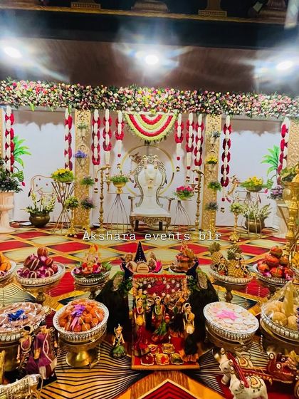 A full view of a grand Seemantham setup, showcasing the main stage, ornate chair, and an extensive display of traditional offerings. The backdrop features red and white floral hangings for a classic look.