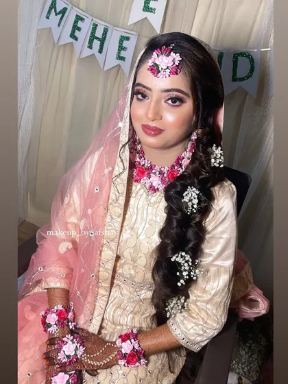 A lovely Mehendi look. This bride is wearing a beautiful cream and pink outfit with matching floral jewellery. The hairstyle is a long, decorated braid.