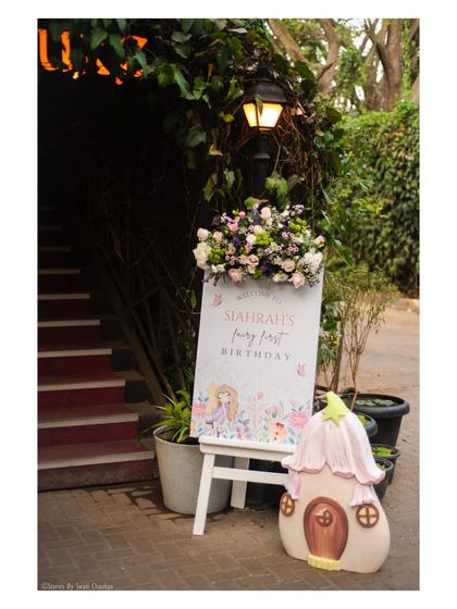 The entrance to the fairy party, featuring a custom welcome sign on an easel, topped with a beautiful floral arrangement and flanked by a whimsical mushroom house prop.