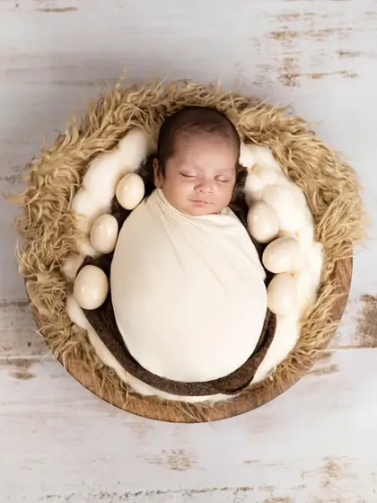 An overhead shot of a newborn sleeping in a nest of eggs. The white wooden background provides a clean, rustic contrast to the natural textures of the props.
